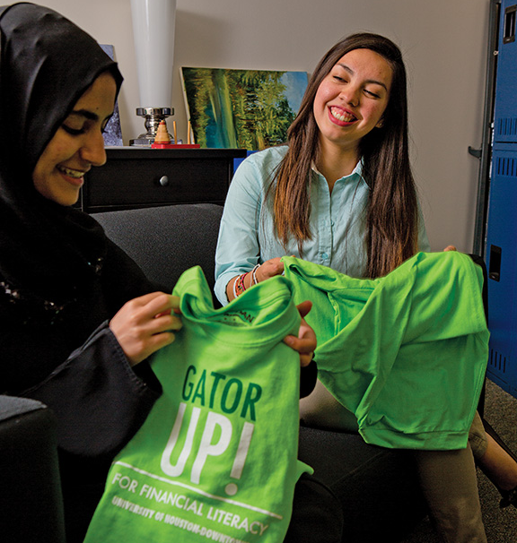 Two smiling students holding neon green shirts that say "Gator Up for financial literacy."